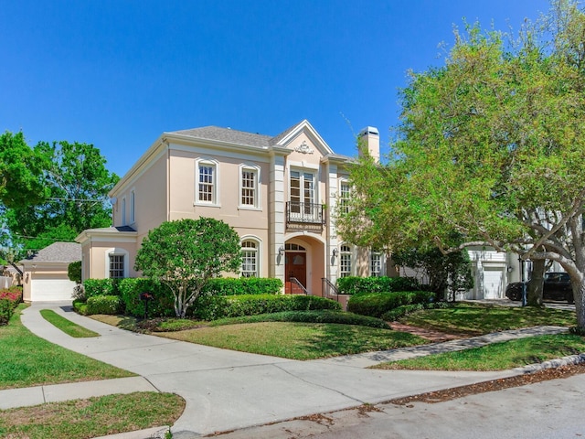 view of front of home featuring a balcony, stucco siding, a garage, a front yard, and a chimney