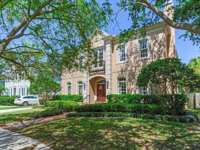 view of front of property featuring a balcony, a front yard, and stucco siding
