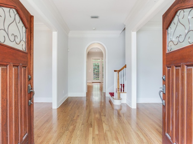 foyer entrance featuring arched walkways, crown molding, light wood finished floors, and baseboards