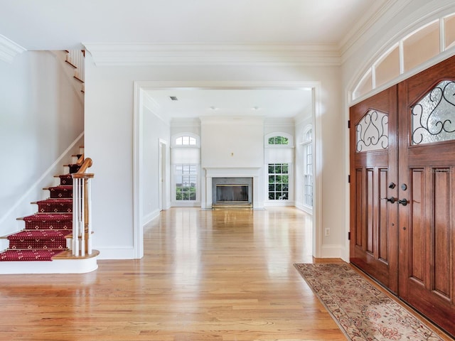foyer with light wood-type flooring, stairway, crown molding, baseboards, and a glass covered fireplace