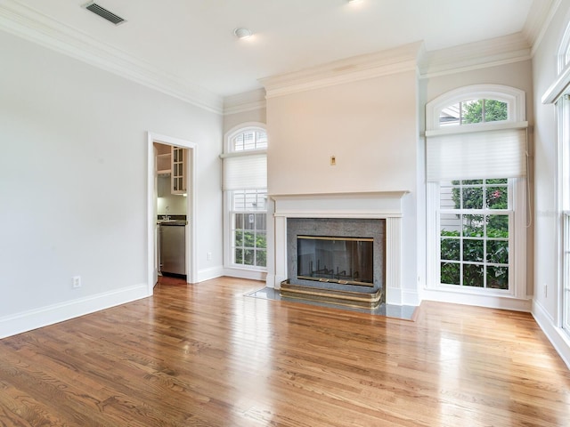unfurnished living room featuring crown molding, a high end fireplace, plenty of natural light, wood finished floors, and baseboards