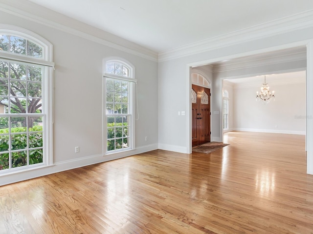 unfurnished room featuring a chandelier, light wood-type flooring, crown molding, and baseboards