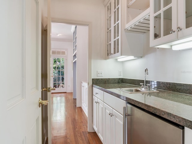 kitchen with a sink, dishwasher, wood finished floors, dark countertops, and white cabinets