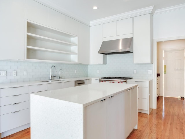 kitchen with wall chimney exhaust hood, a sink, white cabinetry, crown molding, and a center island