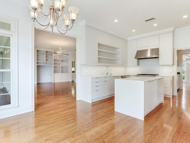 kitchen featuring wall chimney range hood, a chandelier, open shelves, white cabinets, and ornamental molding