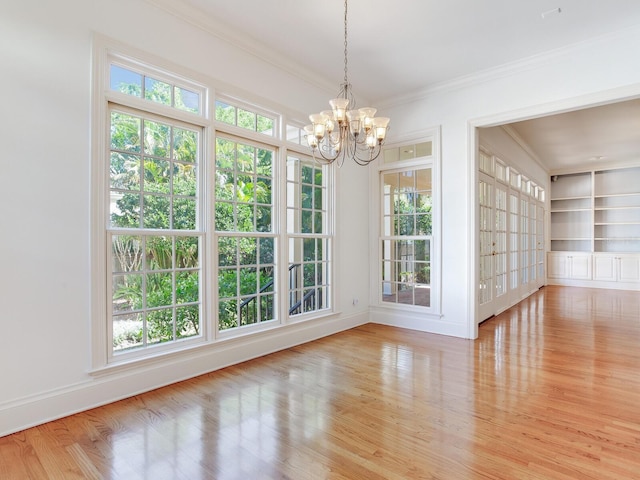 unfurnished dining area featuring ornamental molding, a chandelier, plenty of natural light, and wood finished floors