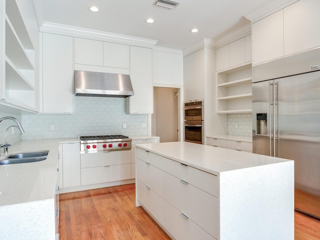 kitchen with appliances with stainless steel finishes, wall chimney exhaust hood, open shelves, a sink, and light wood finished floors