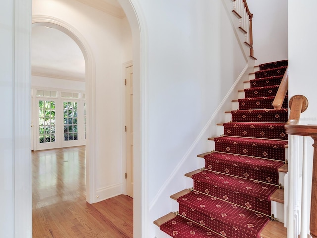 stairway featuring arched walkways, wood finished floors, crown molding, and baseboards