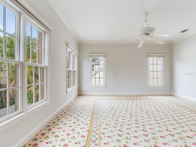 spare room featuring healthy amount of natural light, baseboards, ornamental molding, light colored carpet, and a ceiling fan