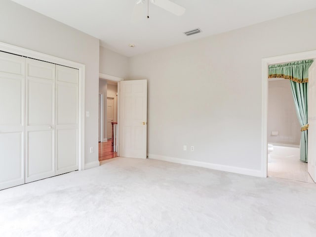 unfurnished bedroom with light carpet, a closet, baseboards, ensuite bathroom, and ceiling fan