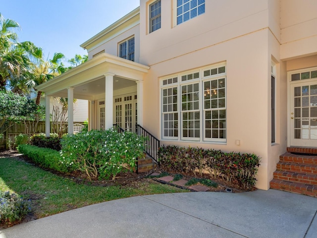 doorway to property featuring covered porch, stucco siding, and fence