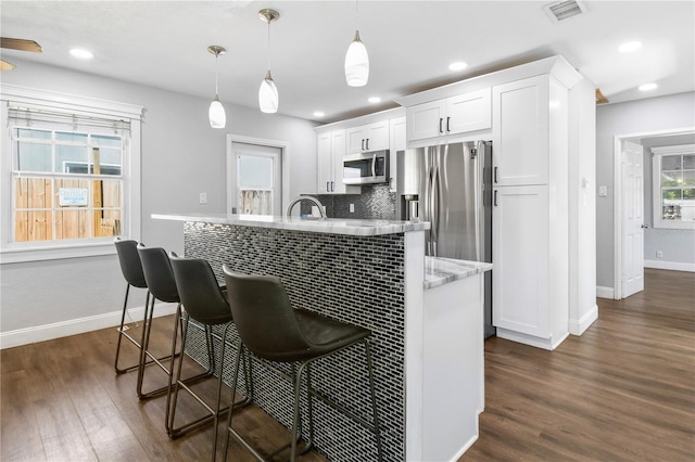 kitchen with white cabinets, a breakfast bar, dark wood finished floors, tasteful backsplash, and appliances with stainless steel finishes