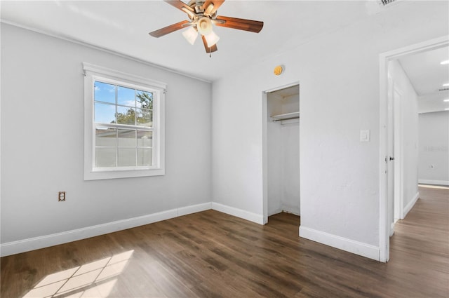 unfurnished bedroom featuring attic access, dark wood-type flooring, baseboards, ceiling fan, and a closet