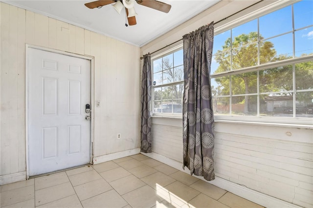 foyer featuring wood walls, crown molding, light tile patterned floors, baseboards, and a ceiling fan