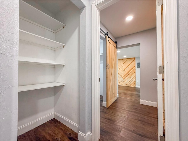 corridor featuring dark wood finished floors, baseboards, a barn door, and recessed lighting
