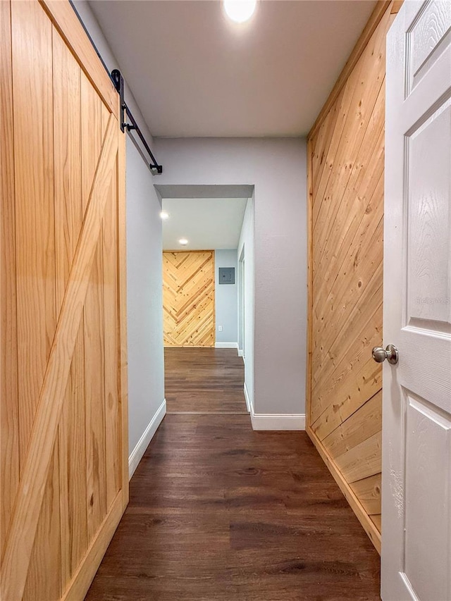 hall with baseboards, a barn door, wood walls, and dark wood finished floors