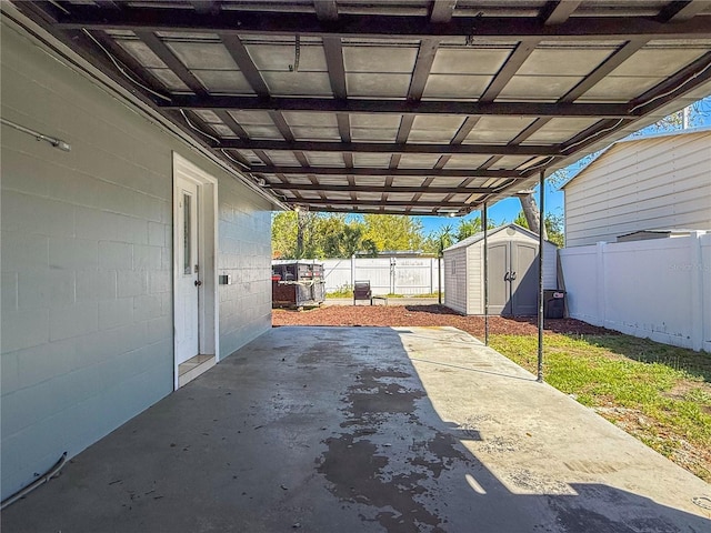 view of patio / terrace with a storage unit, a carport, a fenced backyard, and an outbuilding