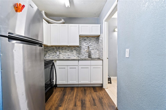 kitchen with backsplash, a sink, stone countertops, freestanding refrigerator, and white cabinetry