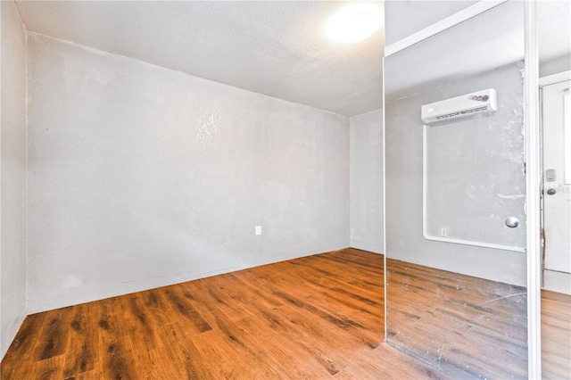 empty room with a textured ceiling, wood finished floors, and a wall unit AC