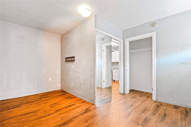 unfurnished bedroom featuring a closet, a textured ceiling, a textured wall, and light wood finished floors