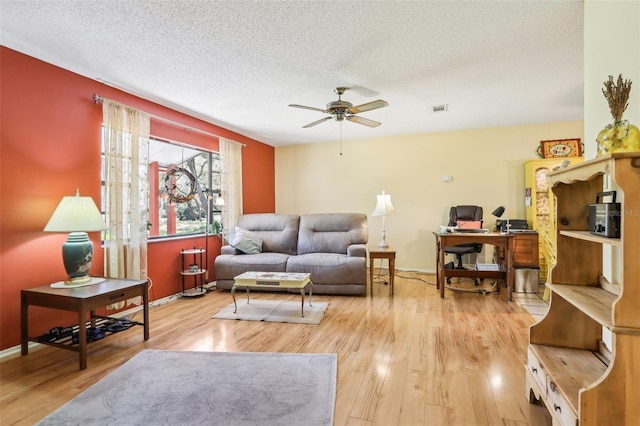 living room featuring baseboards, a textured ceiling, visible vents, a ceiling fan, and wood finished floors