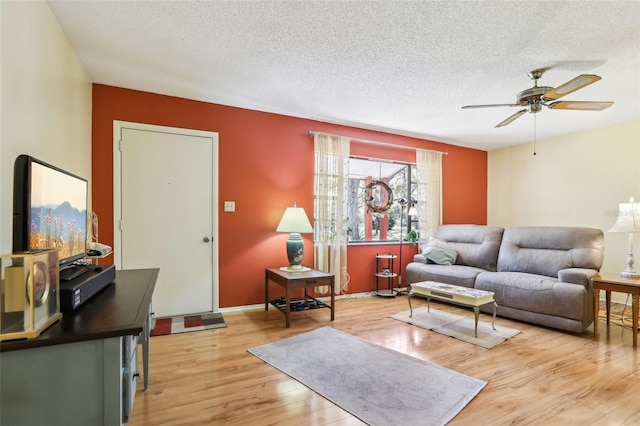 living area with a textured ceiling, light wood-style flooring, baseboards, and a ceiling fan