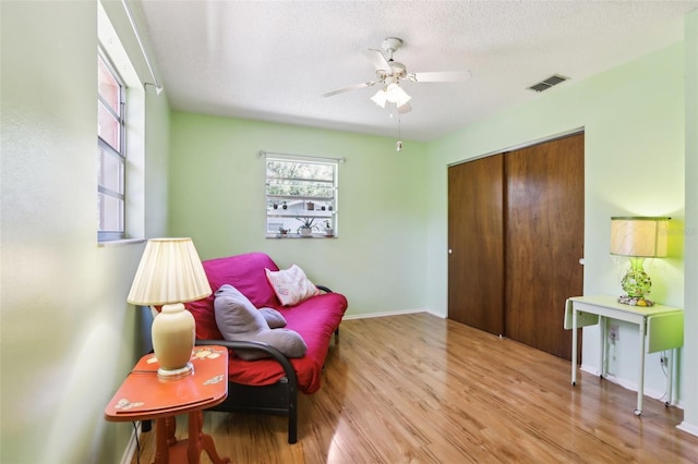 living area featuring a textured ceiling, visible vents, baseboards, ceiling fan, and wood finished floors