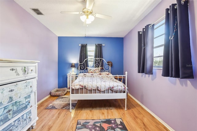 bedroom featuring wood finished floors, baseboards, multiple windows, and visible vents