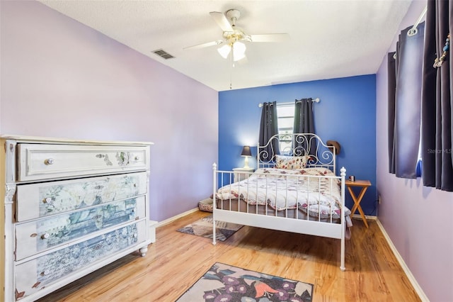 bedroom featuring wood finished floors, a textured ceiling, baseboards, visible vents, and ceiling fan