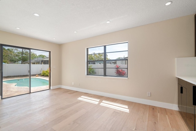 empty room featuring plenty of natural light, light wood-style floors, baseboards, recessed lighting, and a textured ceiling