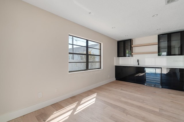 unfurnished living room with wine cooler, baseboards, light wood-type flooring, a sink, and recessed lighting