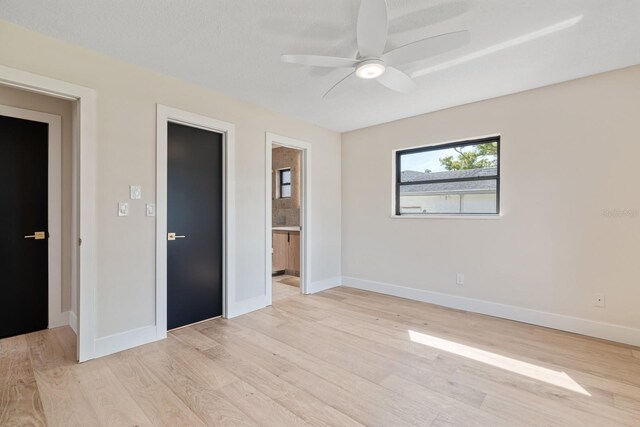 unfurnished bedroom with baseboards, ceiling fan, ensuite bathroom, and light wood-type flooring