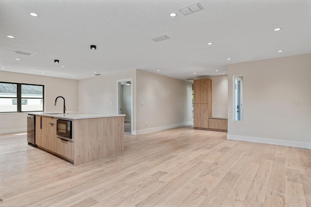 kitchen featuring open floor plan, light brown cabinets, black microwave, a sink, and recessed lighting