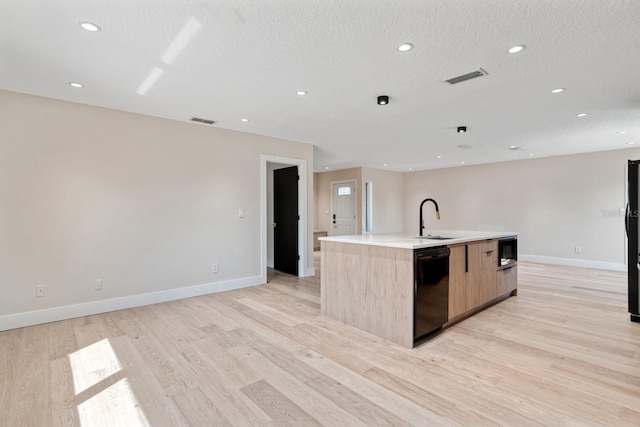 kitchen with black appliances, modern cabinets, light wood finished floors, a kitchen island with sink, and a sink