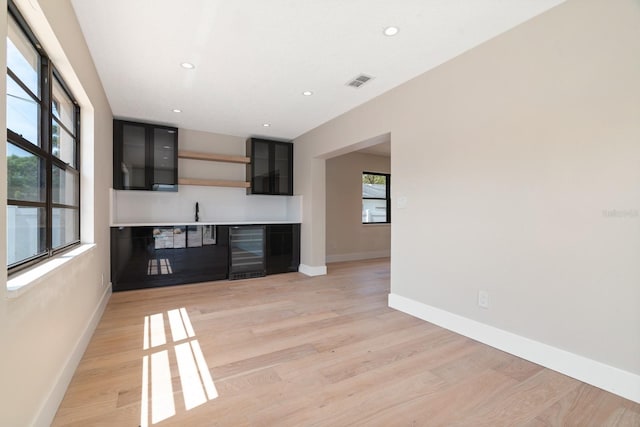 unfurnished living room featuring wine cooler, wet bar, baseboards, light wood finished floors, and recessed lighting