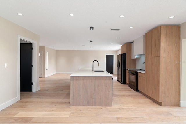 kitchen with black appliances, modern cabinets, a sink, a center island with sink, and baseboards
