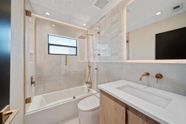 bathroom featuring a textured ceiling, bath / shower combo with glass door, toilet, tile walls, and vanity