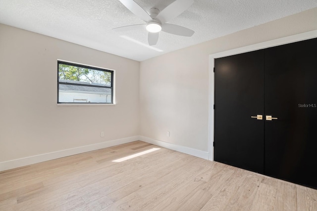 unfurnished bedroom with wood finished floors, a textured ceiling, baseboards, and a ceiling fan