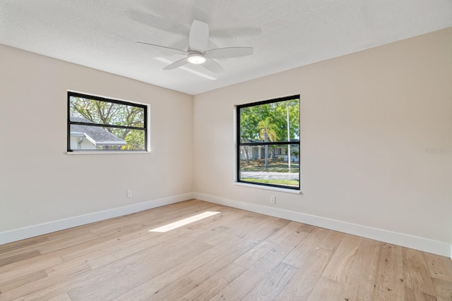 spare room with light wood-style floors, baseboards, a ceiling fan, and a textured ceiling