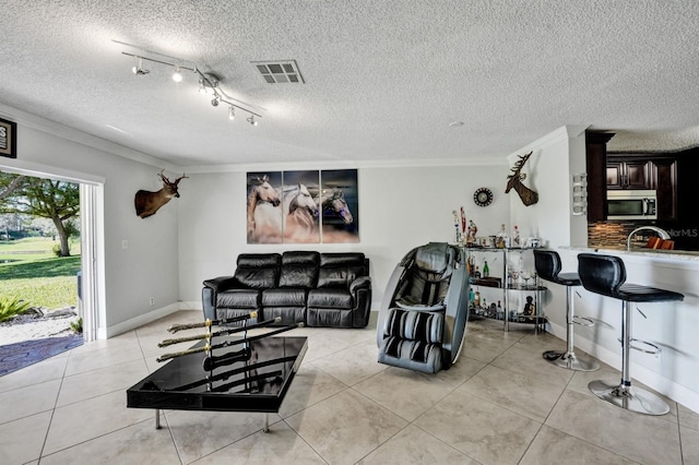 living area featuring a textured ceiling, visible vents, baseboards, ornamental molding, and light tile patterned floors
