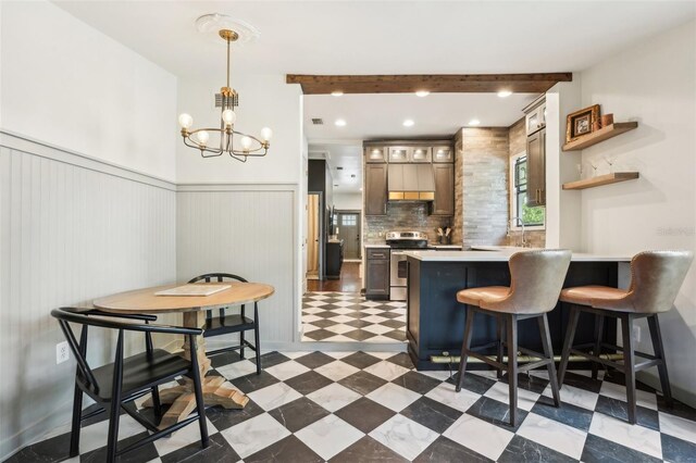 kitchen with a wainscoted wall, a peninsula, stainless steel electric range oven, tile patterned floors, and an inviting chandelier