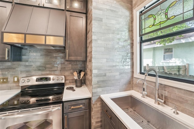kitchen featuring light countertops, exhaust hood, electric range, backsplash, and a sink