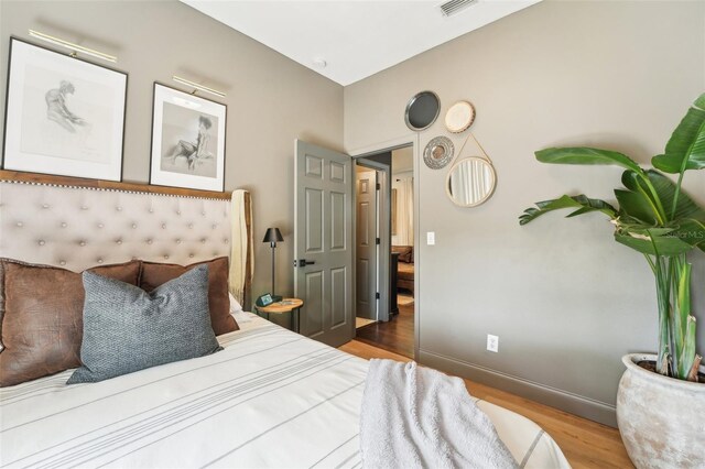 bedroom with baseboards, visible vents, and wood finished floors