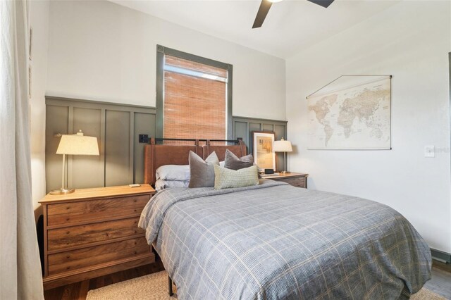 bedroom with a decorative wall, a wainscoted wall, ceiling fan, and wood finished floors