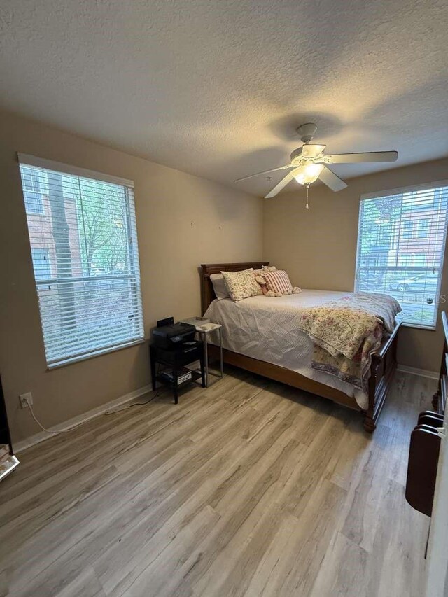 1185 SW 9th Rd Unit 107, Gainesville, FL 32601 - bedroom featuring a textured ceiling, wood finished floors, multiple windows, and a ceiling fan