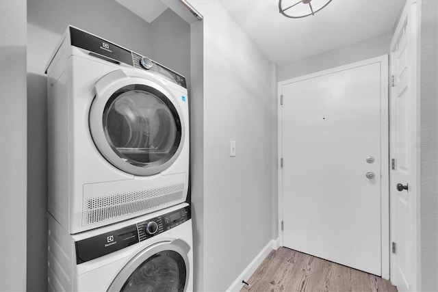 laundry area with baseboards, light wood-type flooring, stacked washing maching and dryer, and laundry area