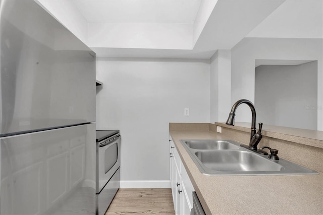kitchen featuring light wood-style flooring, white cabinetry, a sink, freestanding refrigerator, and electric range