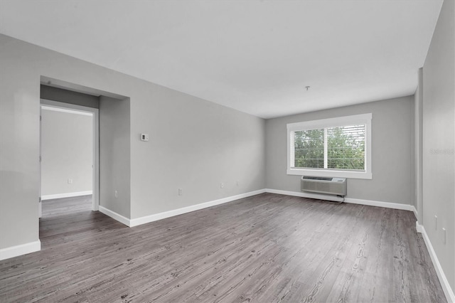 spare room with baseboards, a wall unit AC, and wood finished floors