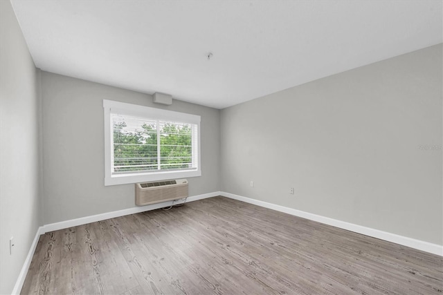 spare room featuring baseboards, wood finished floors, and an AC wall unit