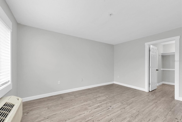 unfurnished bedroom featuring a closet, a wall mounted air conditioner, light wood-style flooring, baseboards, and a spacious closet